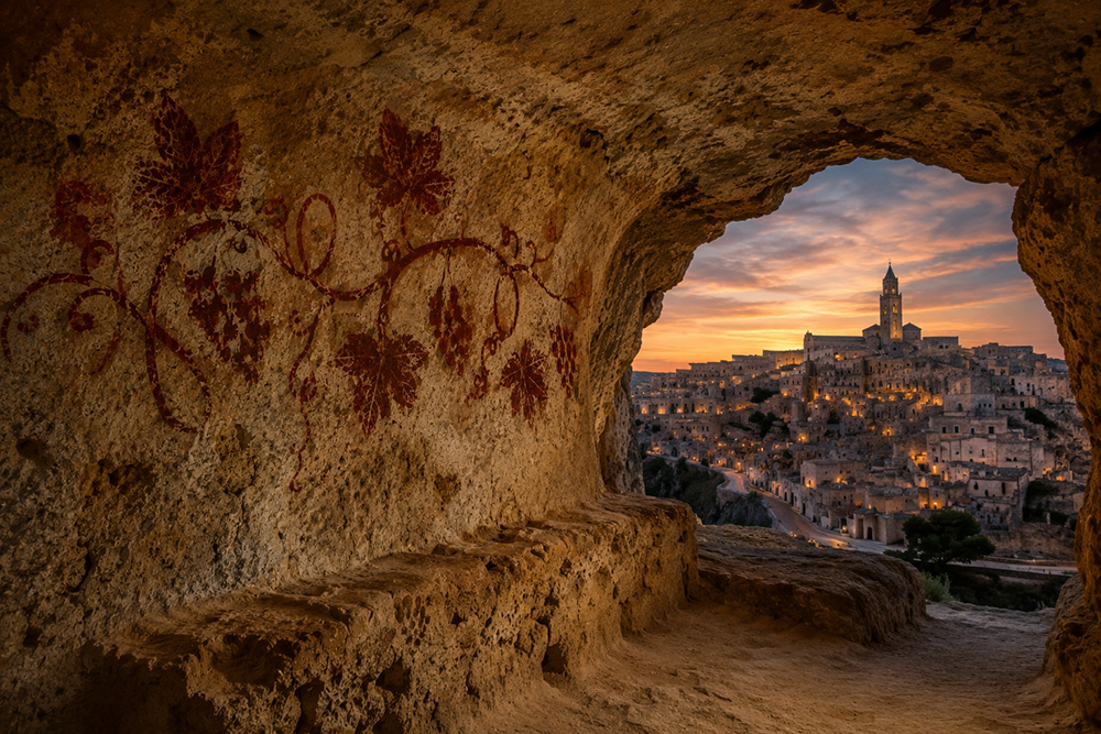 Illustrazione: grotta con un affresco di tralci di vite; dall’apertura, un borgo di pietra al crepuscolo
